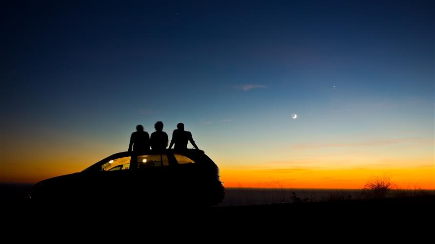 A group of people star gazing on the roof of a car.