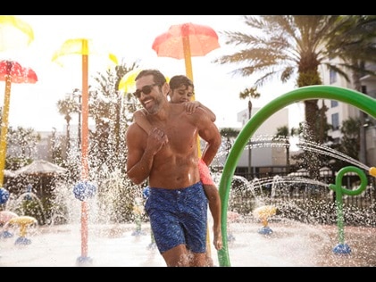Dad and son smiling and playing in the splash pad at Las Palmaras by Hilton Grand Vacations in Orlando, Florida. 