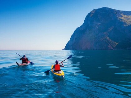 Two people paddling in the Pacific ocean with Hawaii's mountians in the distance.
