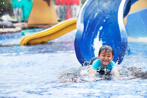 Little boy laughing coming down waterslide. 