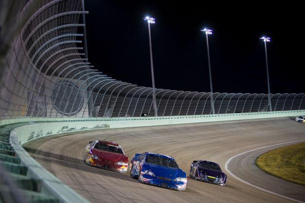 Stock cars driving around a curve on race track.