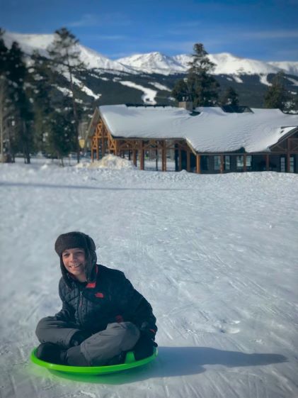 A smiling child rides on a sled down a snowy slope