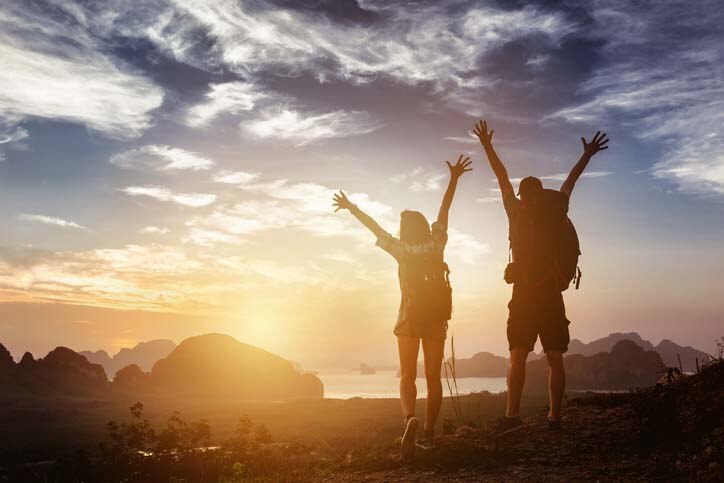 Hikers raising their hands above head in victory on a mountain peak in Hawaii.